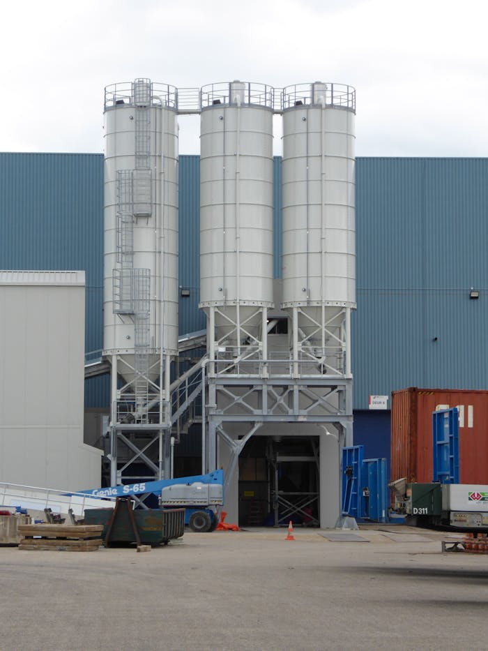 Three large industrial silos with surrounding containers at a warehouse complex.
