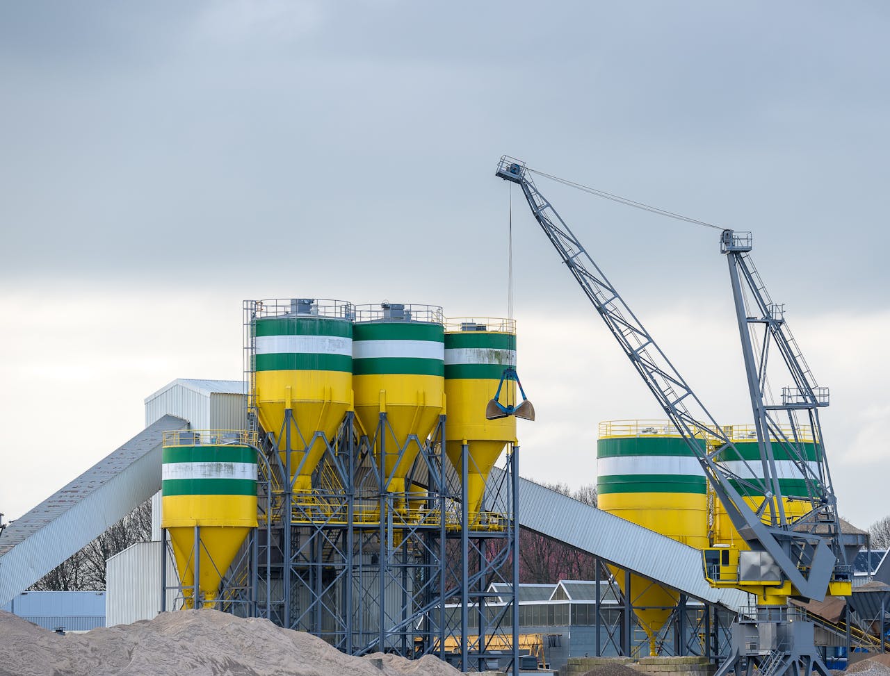 A large industrial crane working with silos at a modern cement plant under cloudy skies.